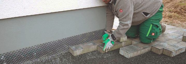 Ein Handwerker verlegt Pflastersteine an einer Hauswand.